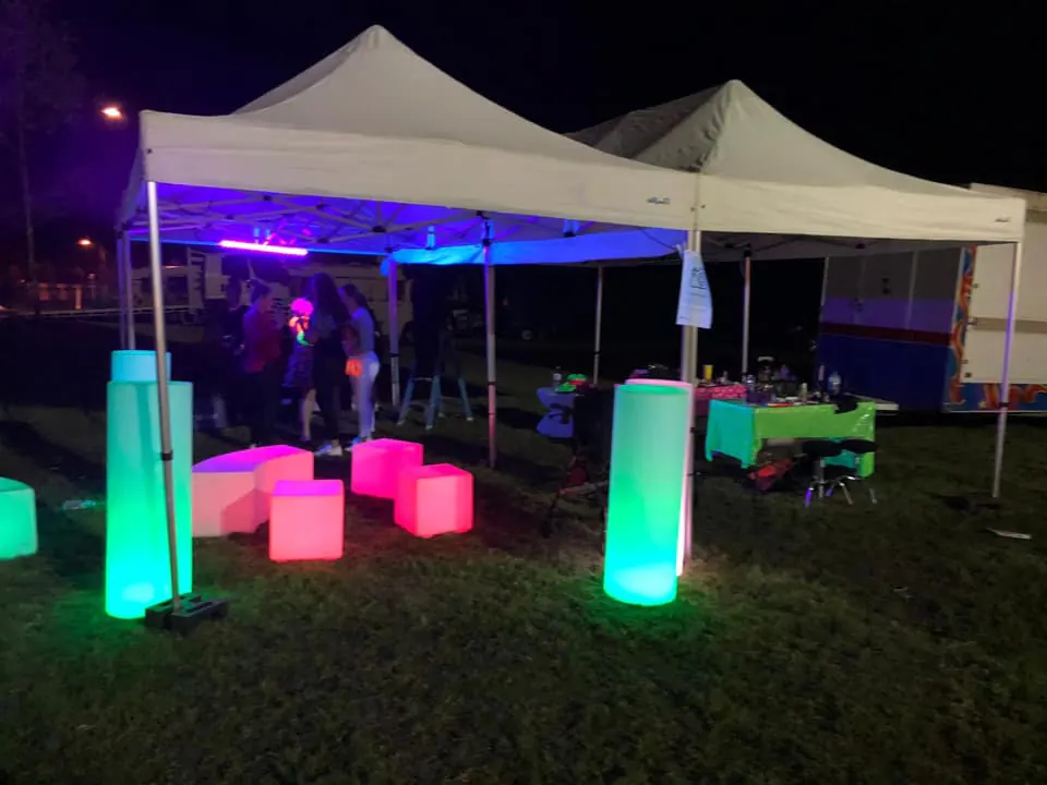 Glow Pillar Hire - A tent with colorful lights and a table in the grass.