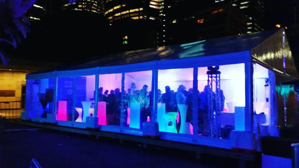 A large tent with people standing in front of it, illuminated by glowing pillars at night.