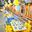 A colorful table set up in a warehouse adorned with vibrant balloons and whimsical tablecloths.