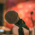 A corded microphone in front of a red wall in a recording studio.