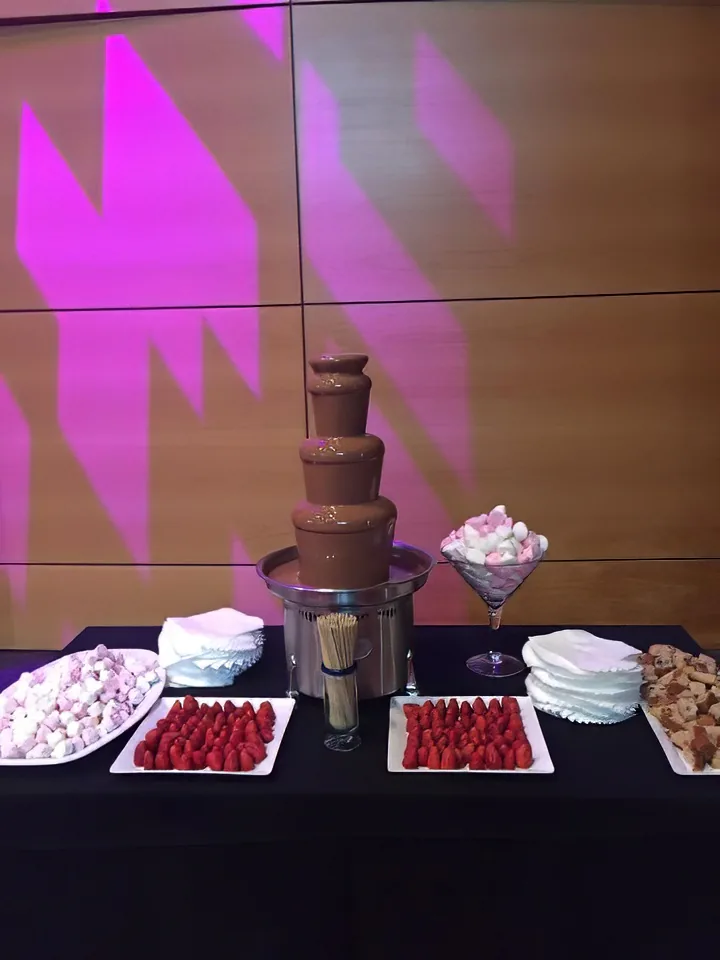 A chocolate fountain on a table with desserts and marshmallows on it.