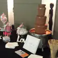 A table with a small commercial chocolate fountain and candy on it.