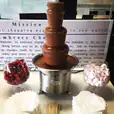 A medium commercial chocolate fountain on a table in a conference room.