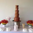 A large commercial chocolate fountain with marshmallows and flowers on a table.