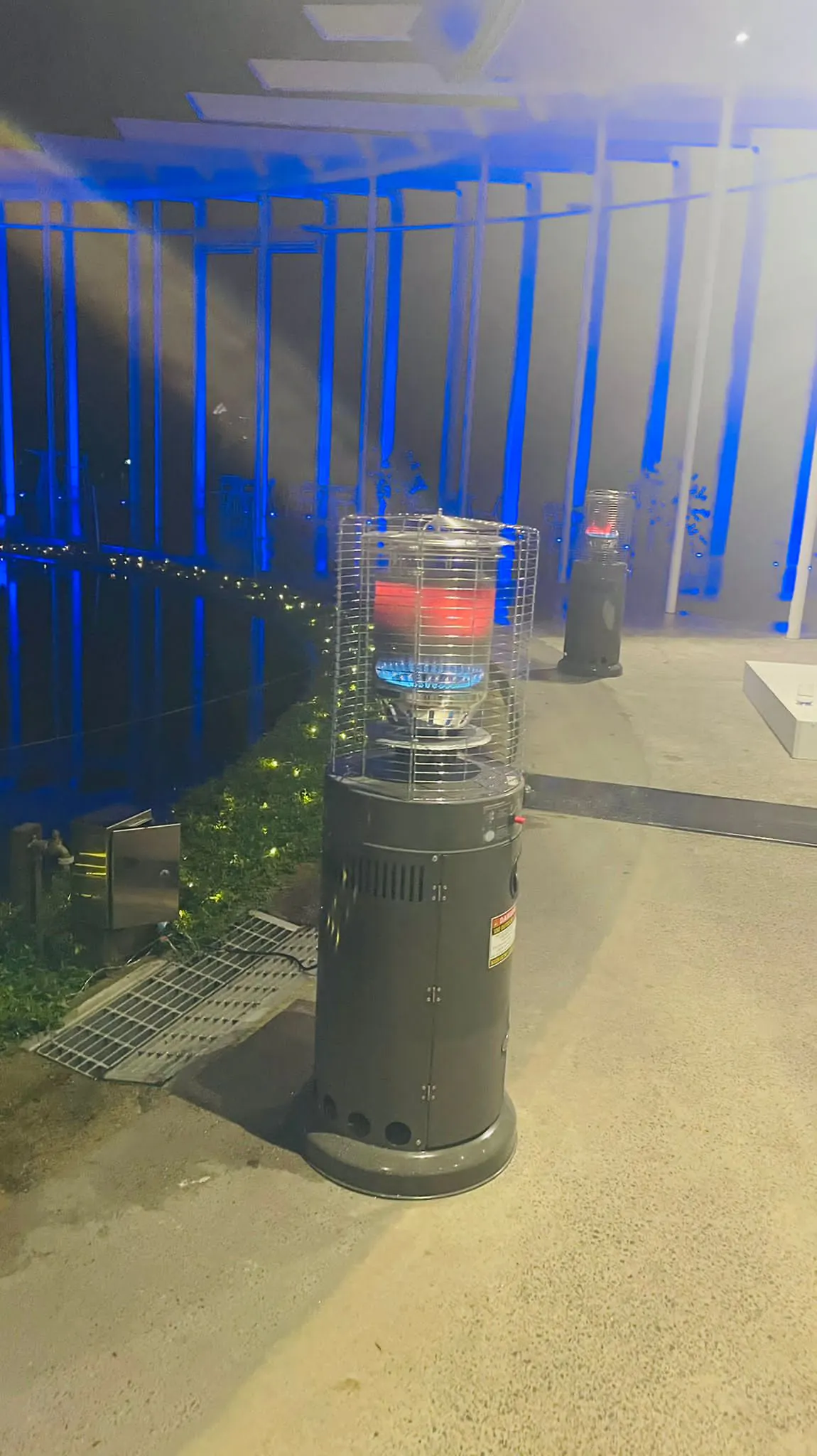 Two gas heaters warming an area in front of a pool at night.