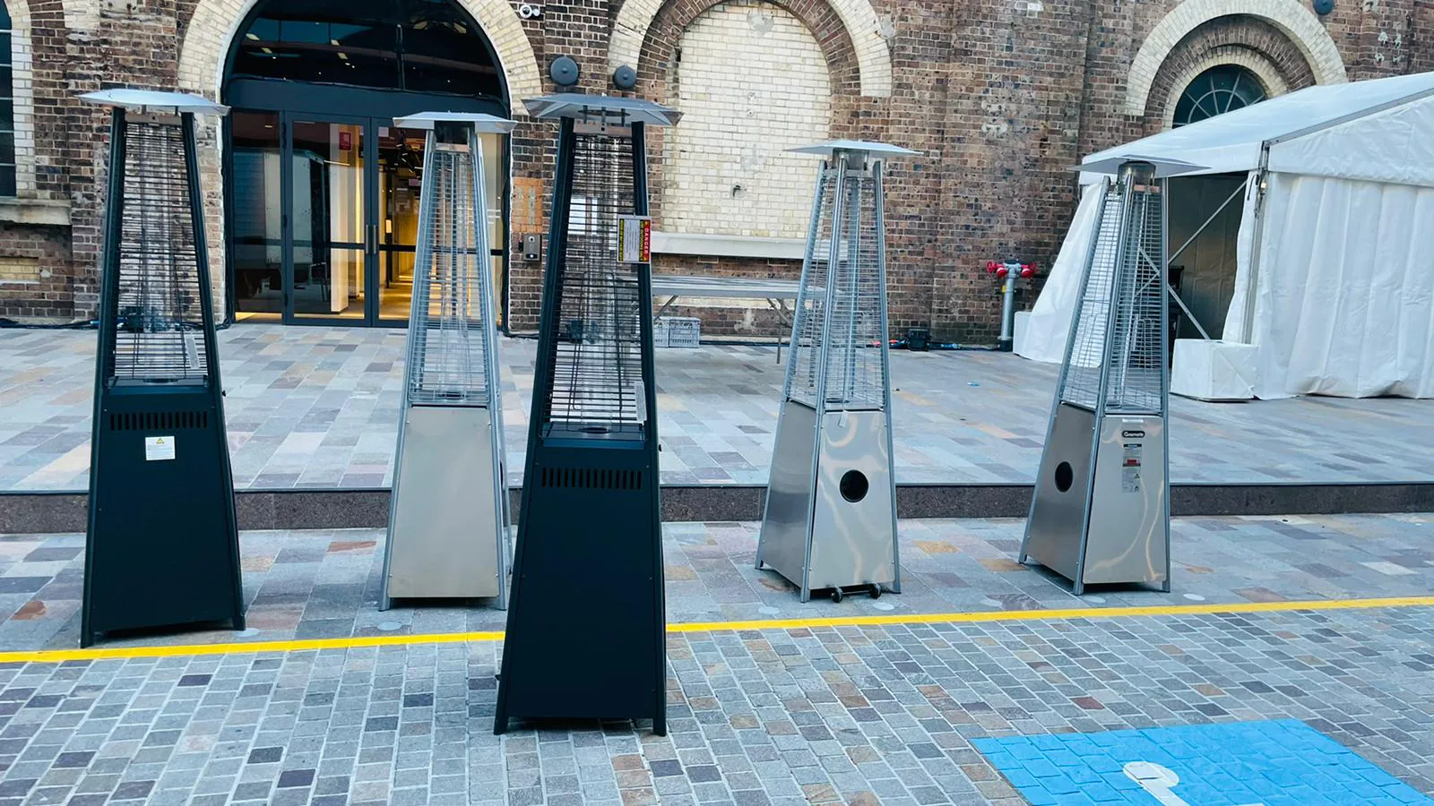 Pyramid heaters are positioned in front of a beautiful brick building, providing warmth and ambiance for outdoor gatherings.