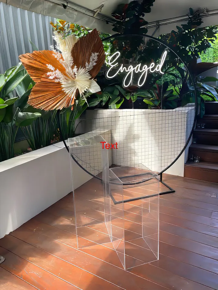 A clear square acrylic plinth hire set of 2, featuring a table embellished with flowers and a sign that says engaged.