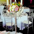A table with silver Tiffany chairs and flowers on it.
