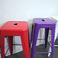 A row of colorful metal stools, including purple Tolix stools, in a room.