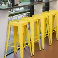 Yellow Tolix Stool Hire - A row of yellow bar stools in front of a window.