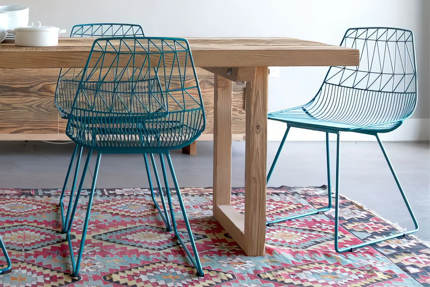 A dining table with turquoise blue chairs and a rug.