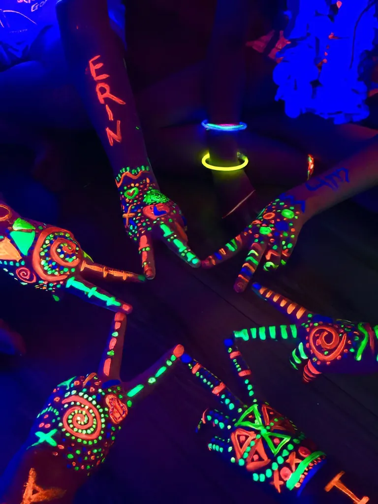 A group of people with glow in the dark paint on their hands illuminated by UV black light.