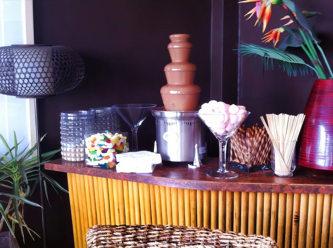 A table with a chocolate fountain and a vase of assorted lollies.