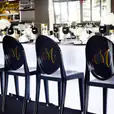 A table with black and white chairs and a Victorian-inspired monogrammed tablecloth.