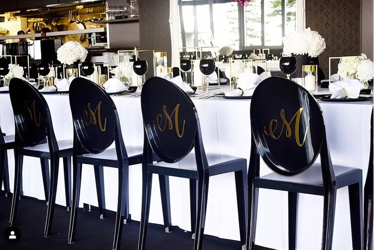 A table with black and white chairs and a Victorian-inspired monogrammed tablecloth.
