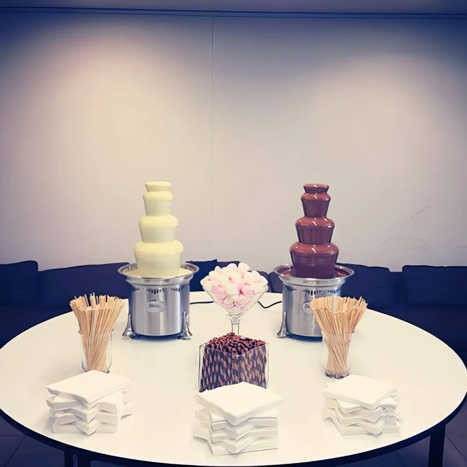 Three chocolate fountains on a table in a conference room, surrounded by wafer biscuits.