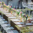 A long table set up with white chairs and flowers, featuring a White Hairpin Banquet Table w/ Timber Top.