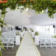 A wedding ceremony set up in a tent with white flowers and greenery, featuring elegant White Padded Folding Chairs (Gladiator chair) for seating.
