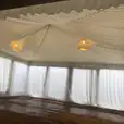 A white tent with white curtains and a wooden floor illuminated by a white pendant rope light.