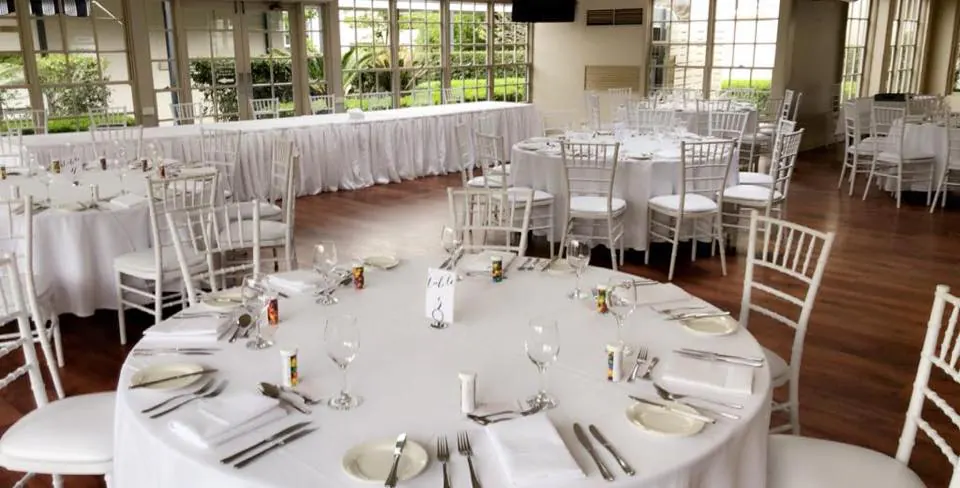 A room with white round banquet tables and chairs set up for a wedding.