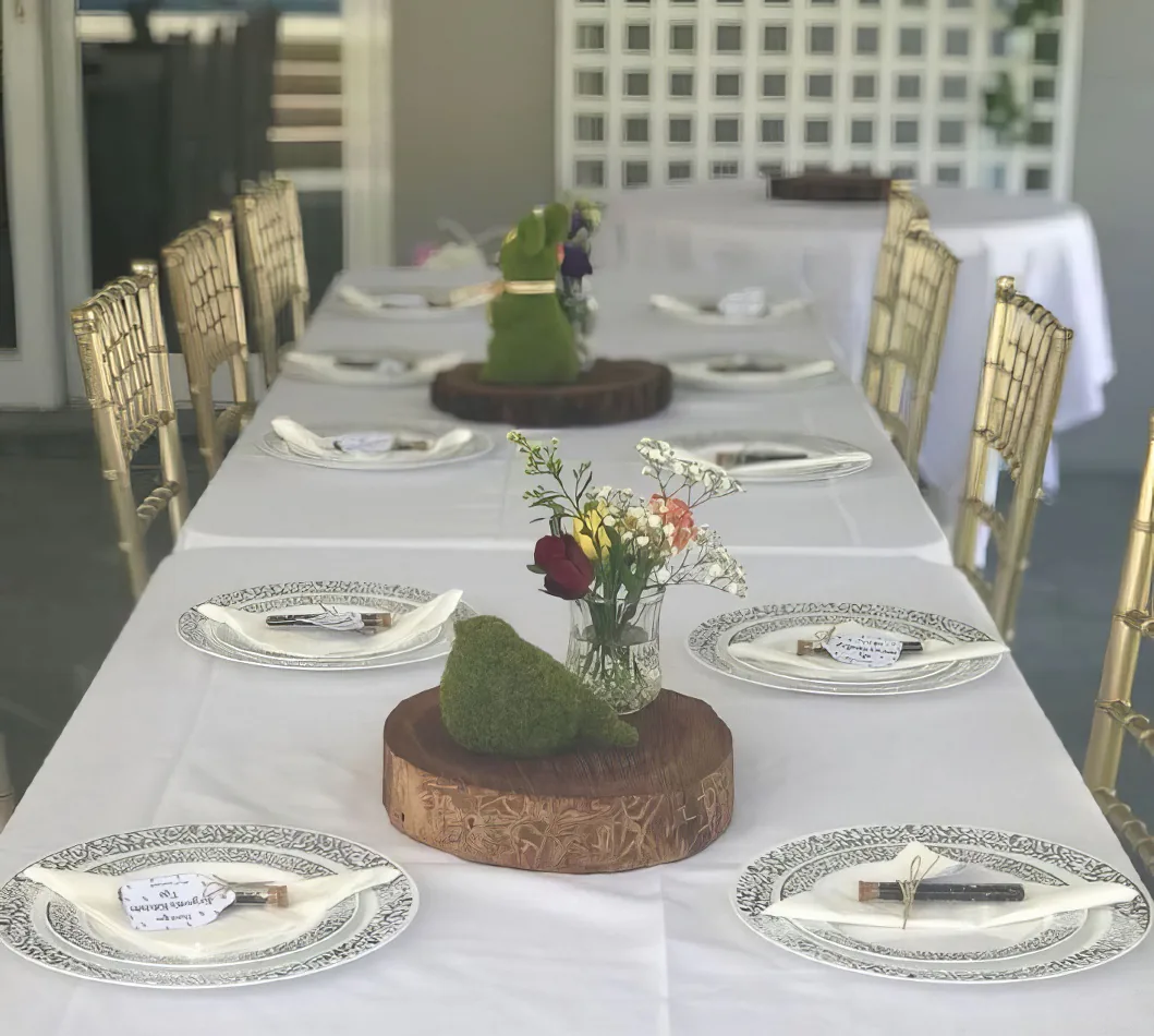 A white tablecloth elegantly drapes over a large trestle table, creating the perfect setup for a dinner party.