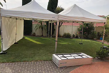 Two connected white pop-up canopies set up on a backyard lawn, with one side wall panel for extra wind and weather protection and open sides for flexible access