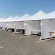 A row of 3mx3m pop-up marquees with walls on three sides erected in a parking lot.