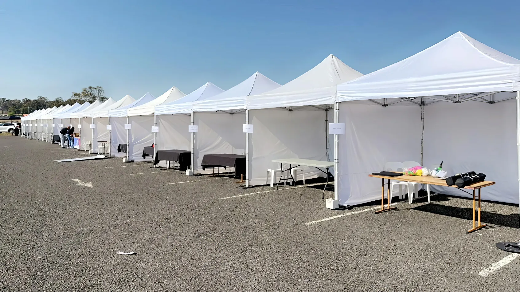 A row of 3mx3m pop-up marquees with walls on three sides erected in a parking lot.