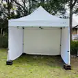 A white 3mx3m pop up tent is set up in a grassy area.