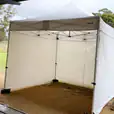 A 3mx3m white tent is sitting on a grassy area with walls on 3 sides.