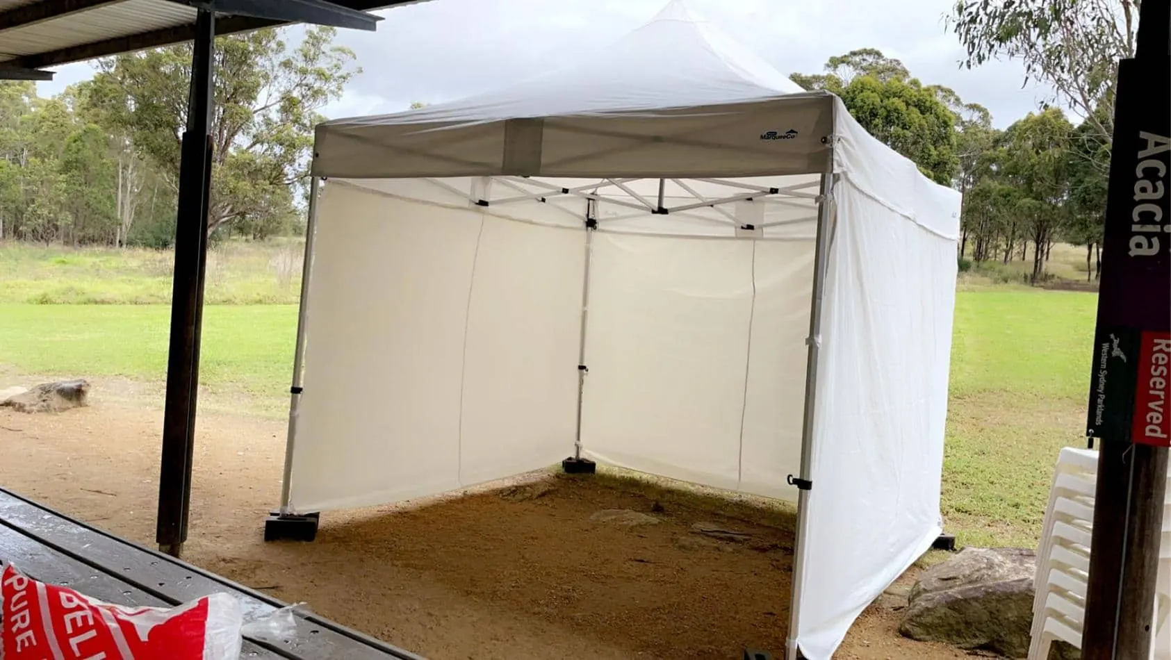 A 3mx3m white tent is sitting on a grassy area with walls on 3 sides.