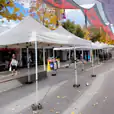 A street lined with 3mx3m pop up marquees, each adorned with a white roof and accompanied by umbrellas.