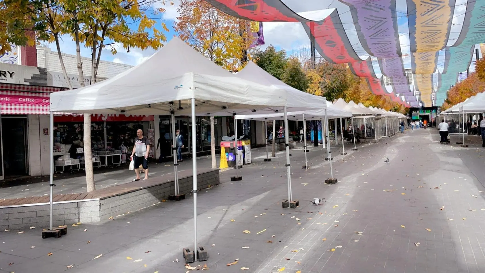 A street lined with 3mx3m pop up marquees, each adorned with a white roof and accompanied by umbrellas.