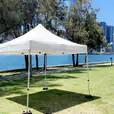 A white tent, the 3mx3m Pop Up Marquee With White Roof, is set up on a grassy area near a lake.