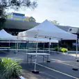 A group of 3mx3m pop up marquees with white roofs set up in front of a building.