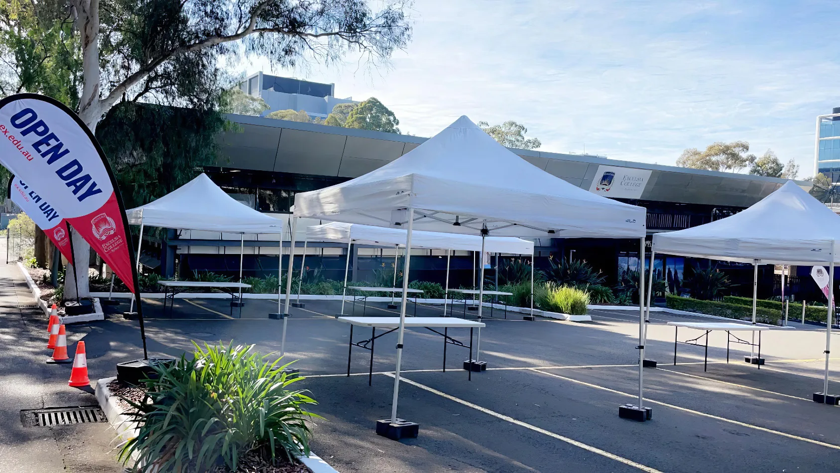 A group of 3mx3m pop up marquees with white roofs set up in front of a building.