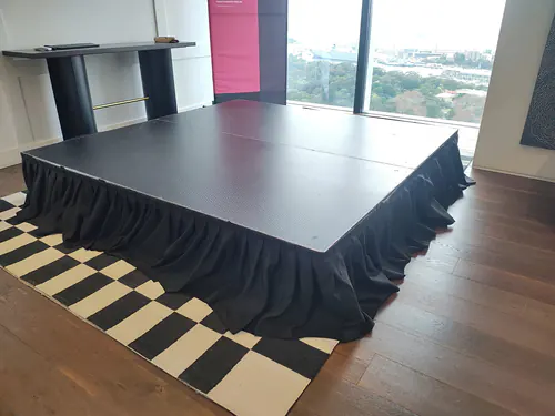 A raised black square stage on a wooden floor