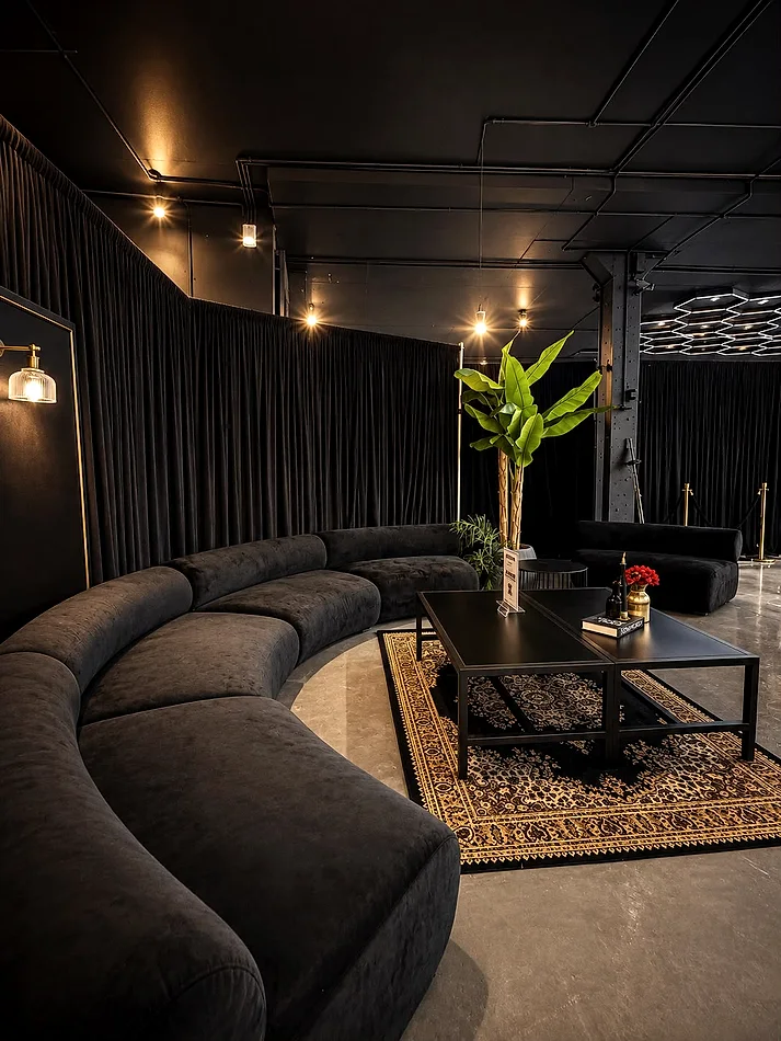 Black draping run the full length of an event space behind a curved black velvet lounge and coffee tables.