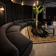 Black draping run the full length of an event space behind a curved black velvet lounge and coffee tables.
