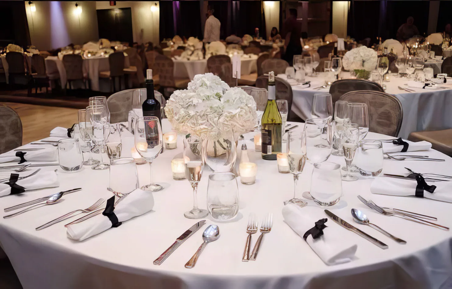 A round black and white table setting with white linens and silverware.