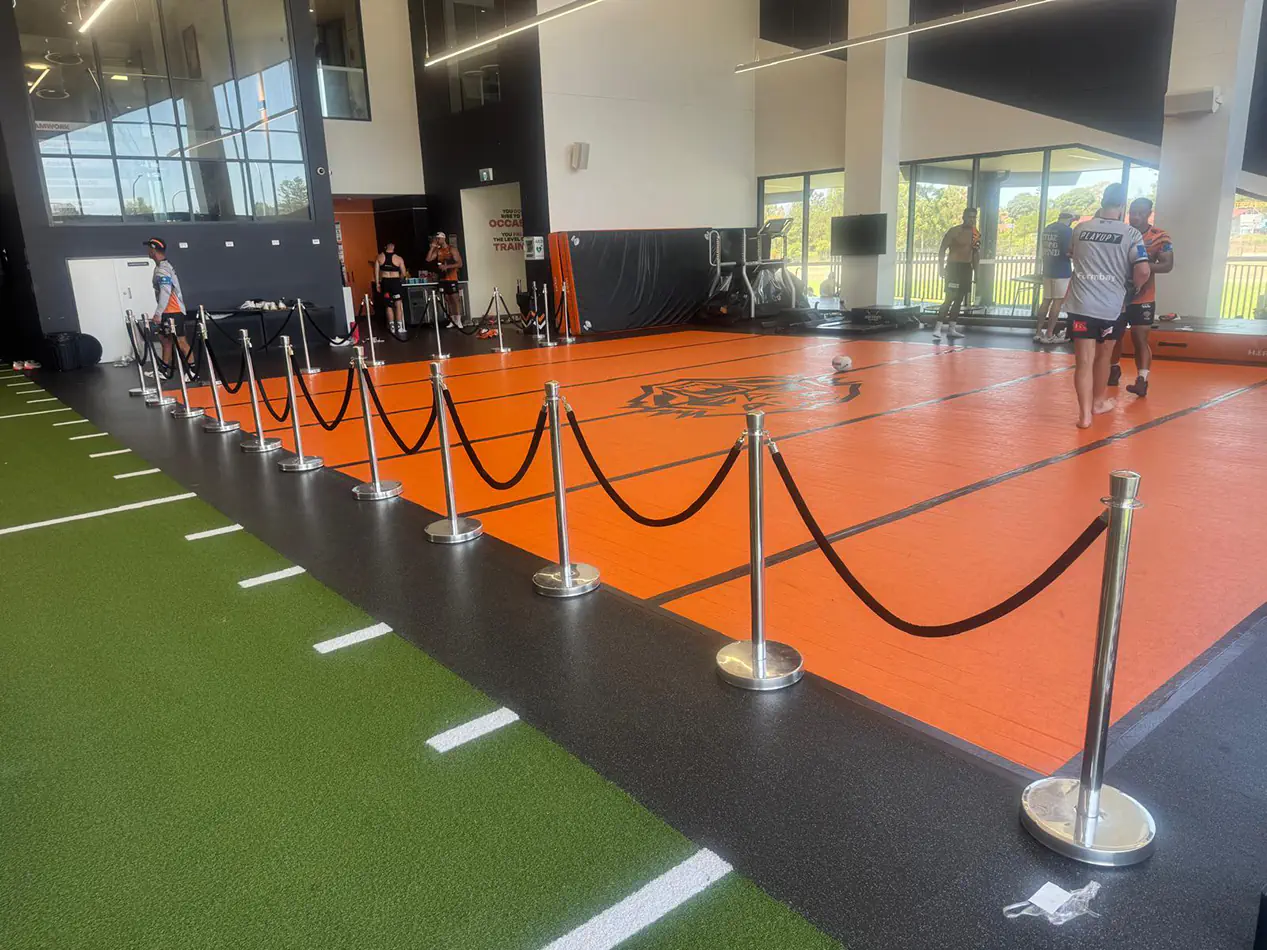 Black velvet bollard ropes and chrome stanchions arranged as crowd barriers around an indoor sports event training area