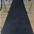 A black carpet runner laid on a light wood floor, flanked by polished silver stanchions connected with black velvet ropes, leading toward a bright room in the background