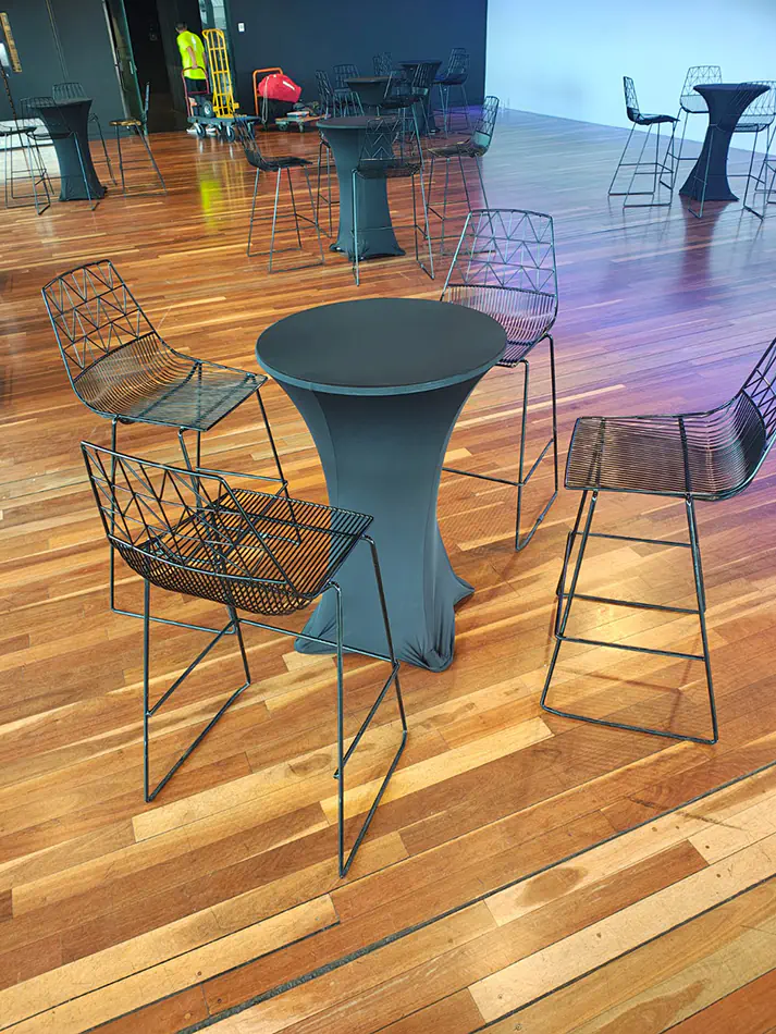 Black cocktail table with fitted black lycra cover surrounded by modern black wire bar stools in an event venue