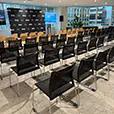 Black conference chairs arranged for a corporate presentation event with stage backdrop, display screens and city office views