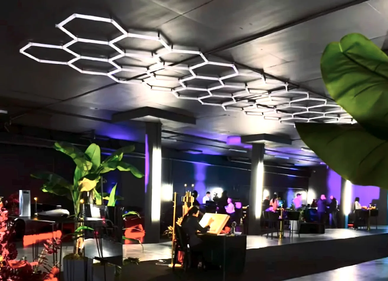 Black draped event space under hexagonal lighting, with cocktail tables and lounge seating set up through the room.