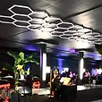 Black draped event space under hexagonal lighting, with cocktail tables and lounge seating set up through the room.