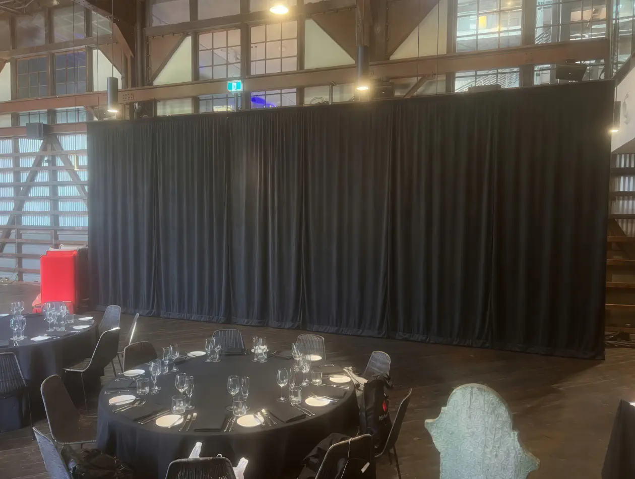 Black event draping used behind round dining tables in a large indoor function space