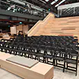 Rows of black folding chairs with padded seats arranged for event seating inside a modern venue with tiered timber steps and open interior space