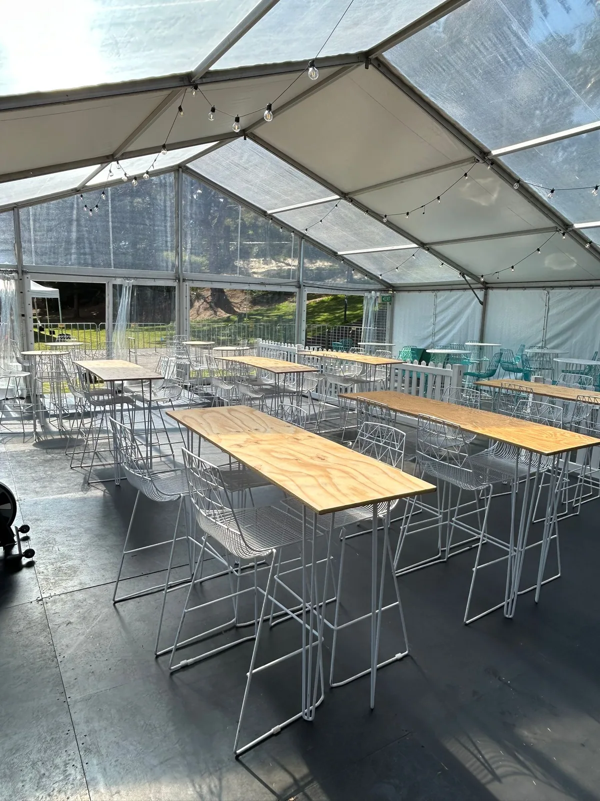 Black hairpin bar tables and stools under festoon lights at an event