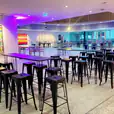 A room with a black hairpin high bar table and stools, adorned with a painting on the wall.